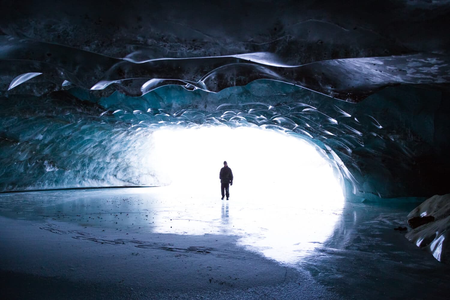 A person stands silhouetted in an icy cave, looking toward a bright light at the entrance.