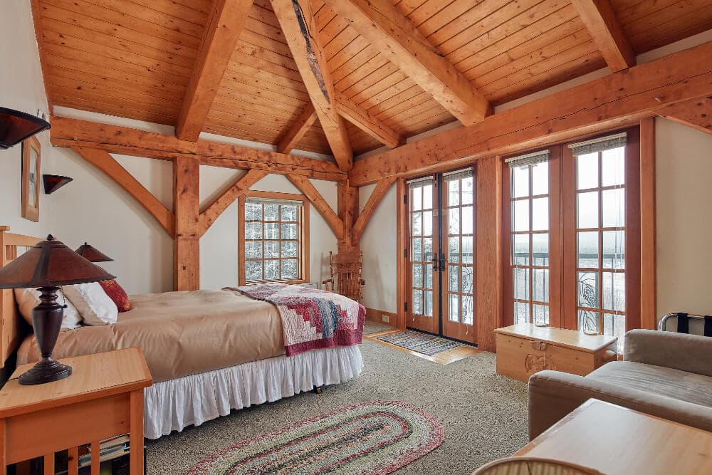 Cozy bedroom with wooden beams, a large window, and a comfortable bed.
