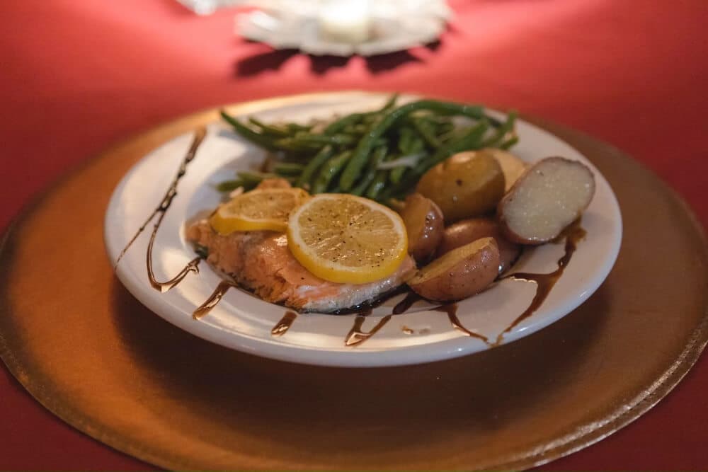 A plated meal of salmon topped with lemon slices, served with green beans and roasted potatoes.